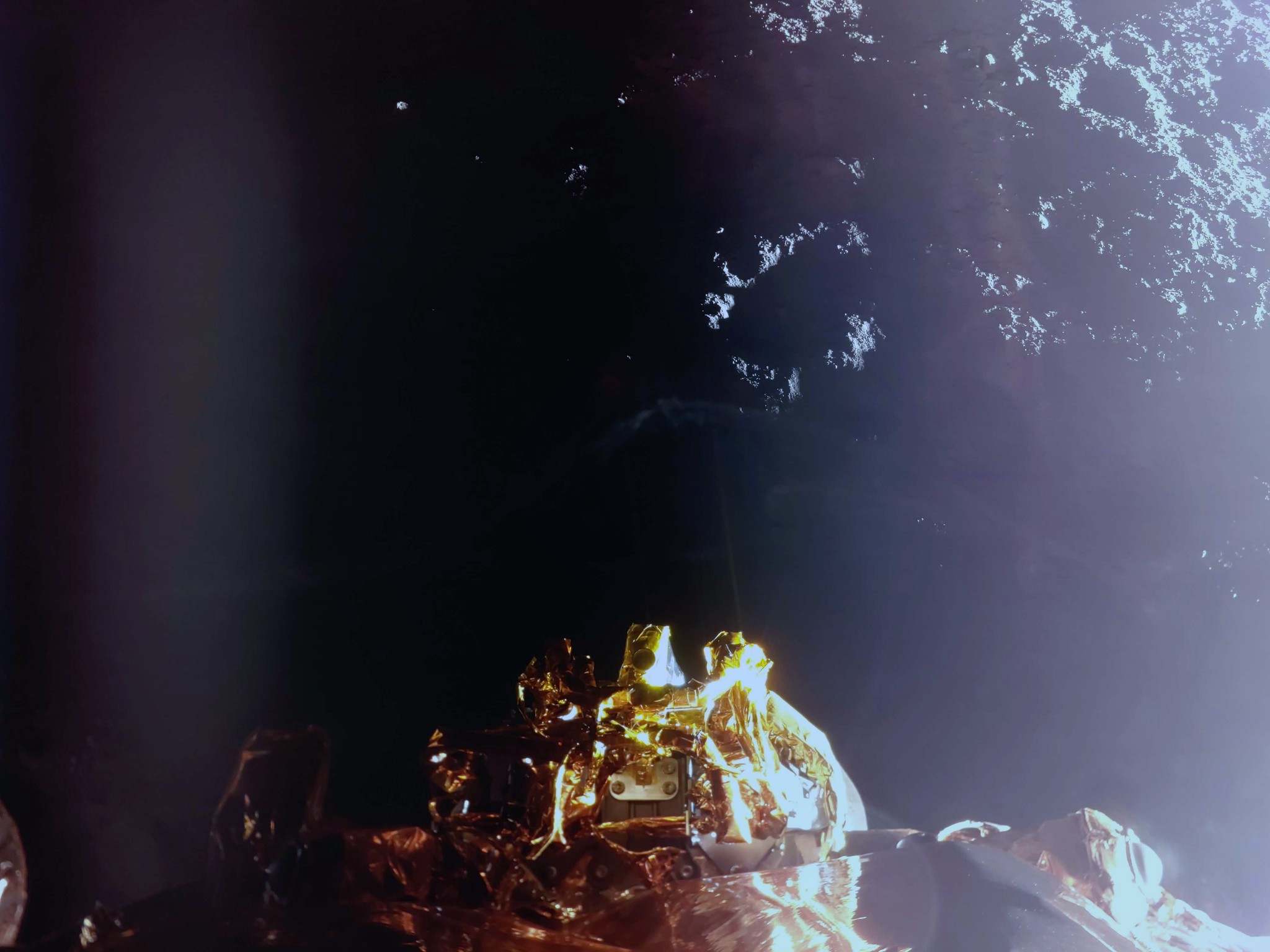 L'image montre la surface de la Lune et une vue plongeante sur les propulseurs RCS du module d'atterrissage (au centre), avec un éblouissement du soleil sur le côté droit.