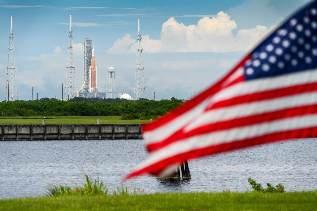 La fusée SLS sur le pas de tir du Kennedy Space Center avec un drapeau américain au premier plan, symbole du spatial américain en pause pendant le shutdown.